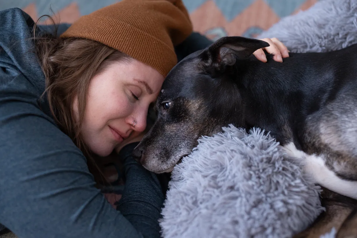 Woman resting her cheek against her senior dog’s head, eyes closed