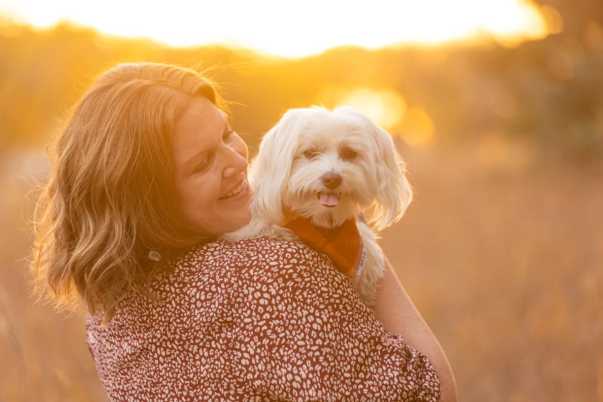 Woman holding her small white dog in golden evening light