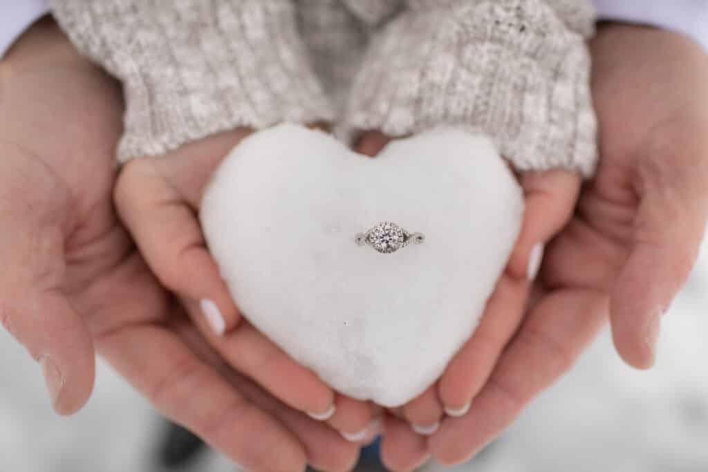 hands together holding heart shaped snowball with diamond ring